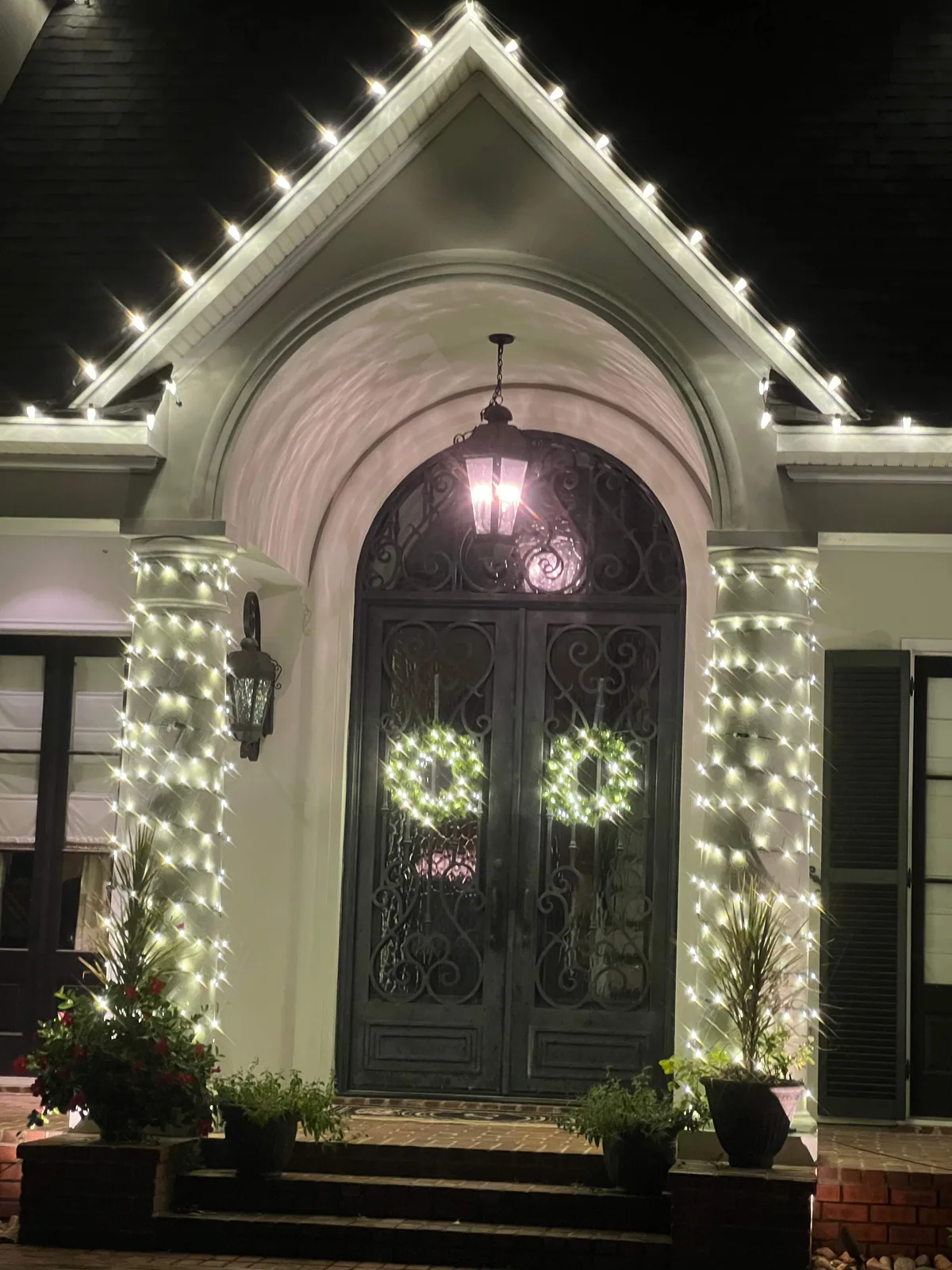 A Christmas entrance with two illuminated wreaths, light-wrapped columns and bulbs outlining the porch gable