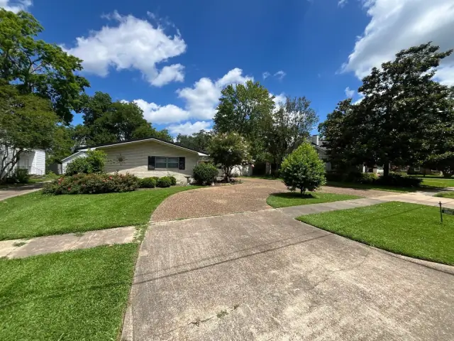 Freshly mowed corner lot with curved beds under a wide cloud-streaked sky