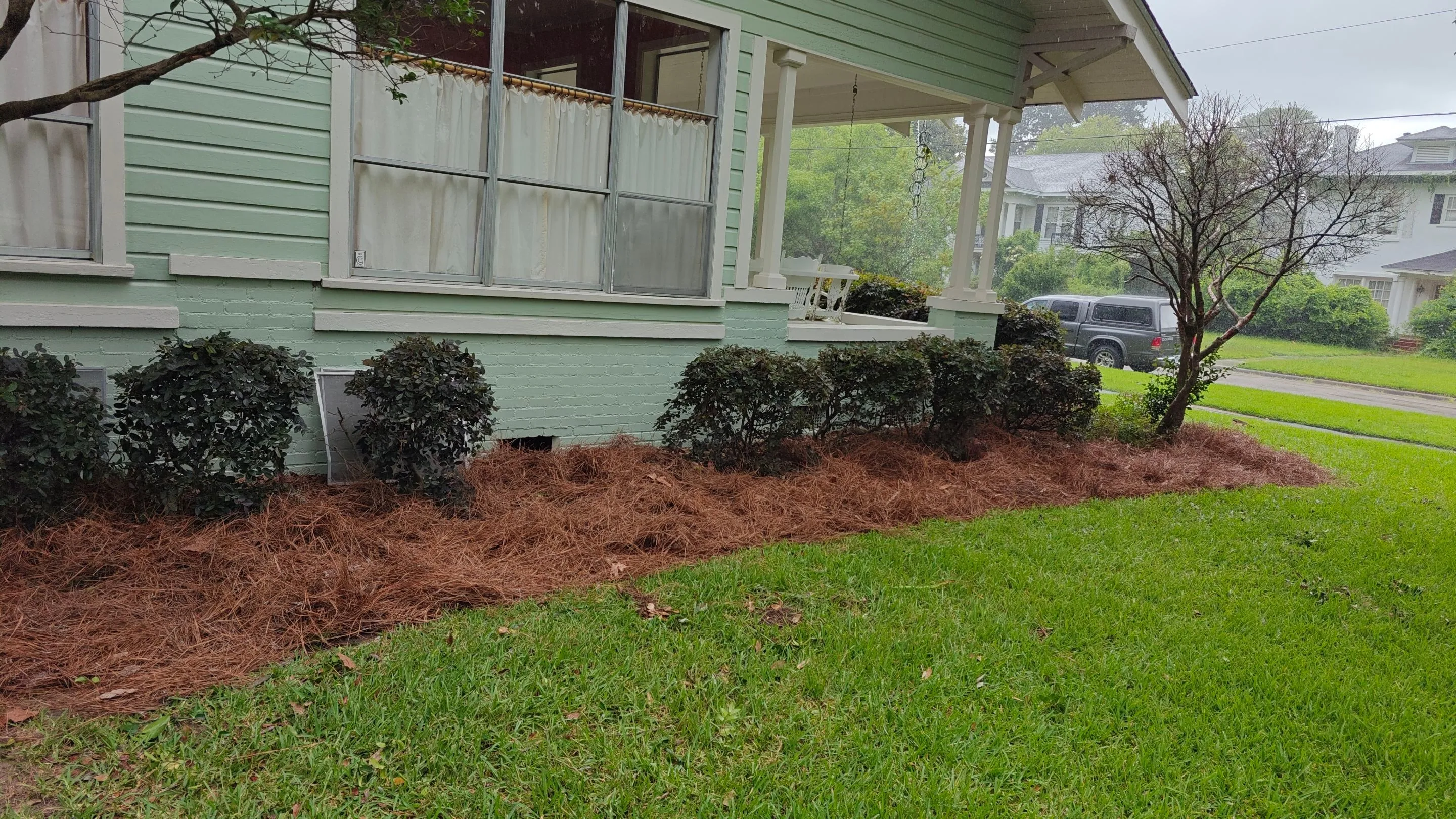 Mulched shrub beds with fresh pine straw wrapping around a front porch beside a green lawn